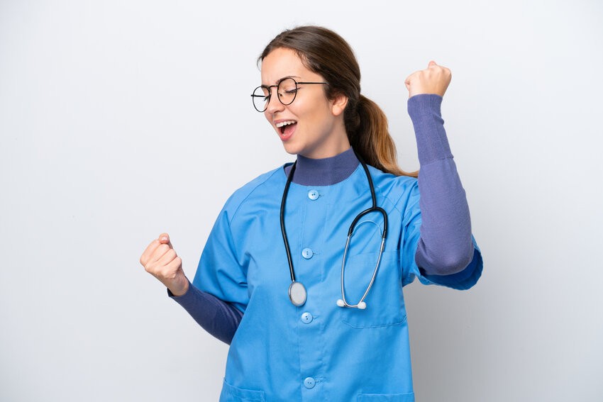 A healthcare professional in blue scrubs and a stethoscope, wearing glasses, raises her fists and smiles with enthusiasm about the MCCQE1 QBank update.