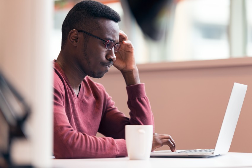 A person in a red sweater works on a laptop at a desk, with a white mug beside them. They are looking at the screen with a thoughtful expression, perhaps contemplating their MCCQE1 prep questions on Ace QBank.