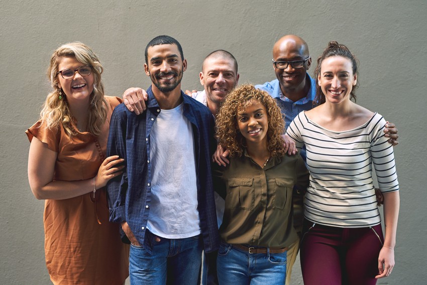 A group of friends smiling and standing close together in front of a plain wall. They have their arms around each other in a friendly manner, embodying the spirit of balancing health and study during their MCCQE1 exam preparation.