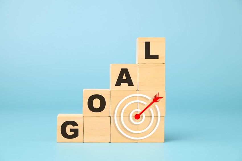 Wooden blocks spelling "GOAL" are stacked in ascending order, with a red dart hitting the bullseye of a target on the front of the blocks, set against a blue background. Avoid procrastination to boost MCCQE1 prep and achieve your goals with Ace QBank.