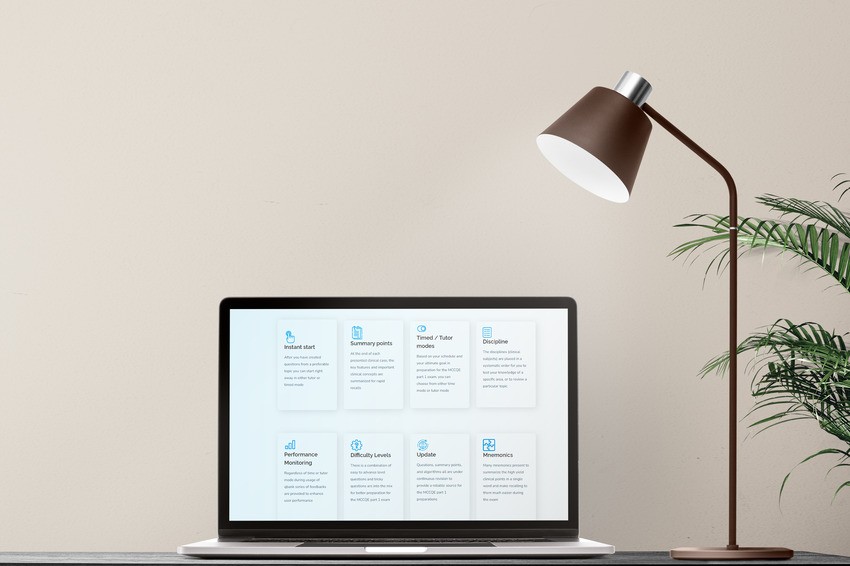 A laptop displaying a digital dashboard with various widgets, including Ace QBank features for MCCQE1 exam preparation, is placed on a desk. A modern desk lamp and a small potted plant are beside it against a neutral wall.