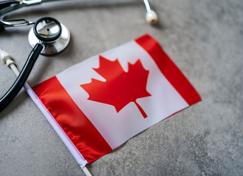 A Canadian flag lies on a grey surface next to a stethoscope, symbolizing healthcare in Canada. Acing MCCQE1 is your key to unlocking a future in this robust system—Ace QBank can help make that journey seamless.