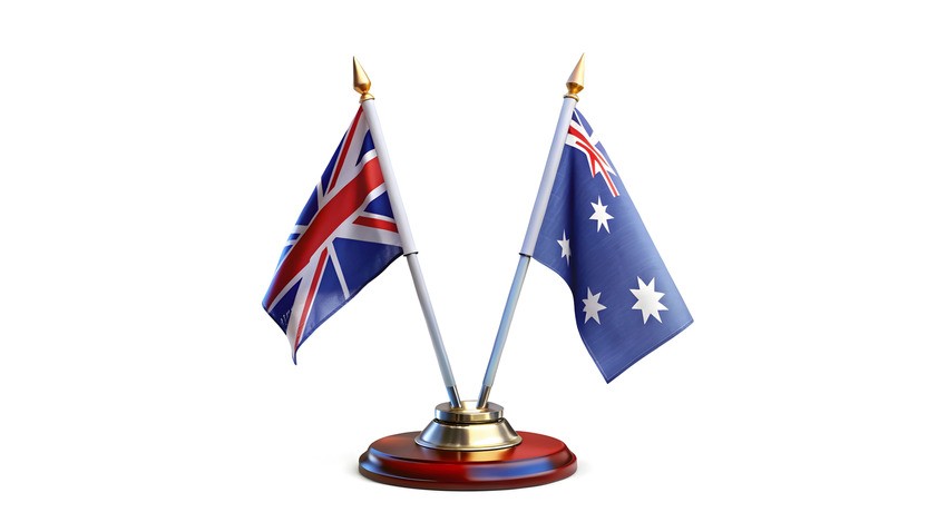 Two miniature flags, one of the United Kingdom and one of Australia, stand proudly on small flagpoles set in a shared, round wooden base with golden accents—a perfect addition to your study desk while preparing for the MCCQE1 exam with Ace QBank.