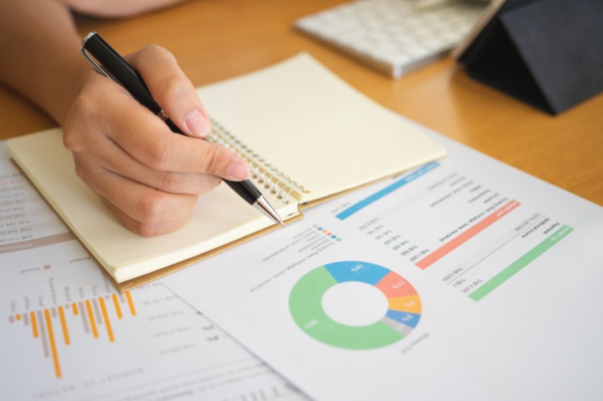 Person holds a pen over a notebook while reviewing charts and graphs on documents placed on a desk, focused on analyzing the MCCQE part 1 pass rate.