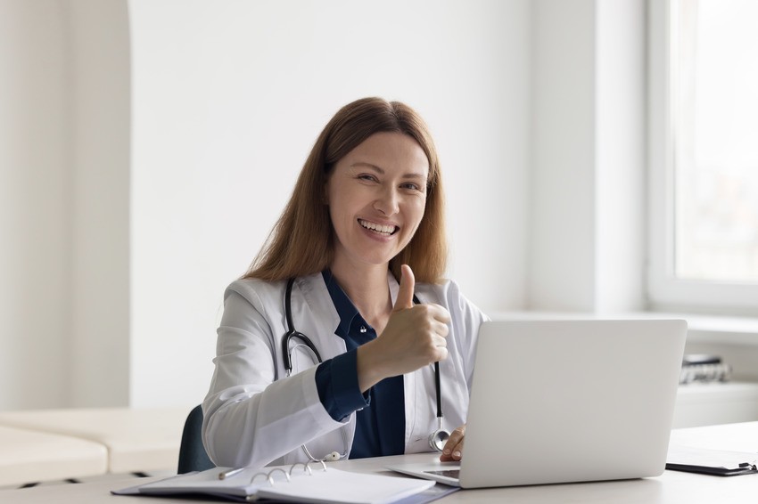 A smiling doctor in a white coat gives a thumbs-up while seated at a desk with their laptop and Ace QBank, ready to tackle the MCCQE1 with confidence.