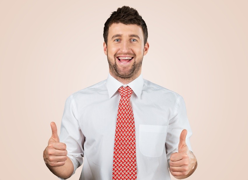 A man in a white shirt and red patterned tie gives two thumbs up, as if triumphantly answering, "Does self-assessment for MCCQE1 matter?", standing against a plain beige background.