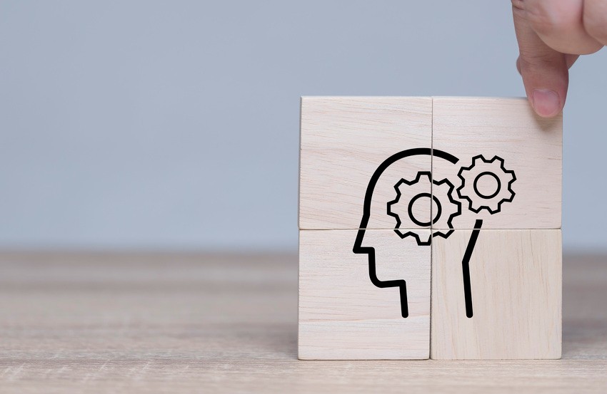 A hand adjusts wooden blocks with a human head outline and gears inside, symbolizing cognitive processes or problem-solving—much like preparing for the MCCQE1 exam with strategic self-assessment using Ace QBank.