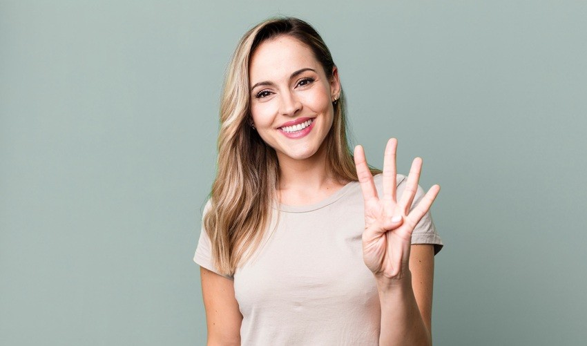 Smiling person holding up four fingers in front of a light green background, celebrating the latest Ace QBank update for MCCQE1 preparation.