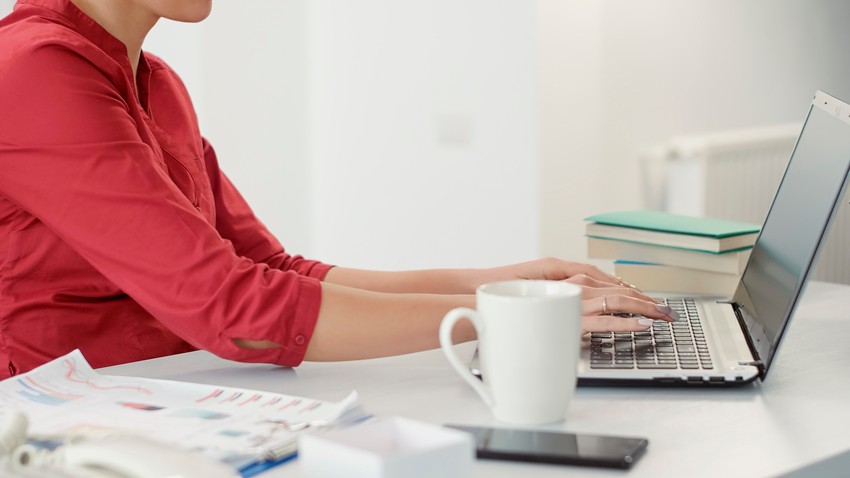 A person in a red shirt intently types on a laptop at a desk surrounded by study materials, including Ace QBank, while exploring tips on "How to Study for MCCQE1 Distraction-Free?" amidst nearby books, a smartphone, and a steaming coffee mug.