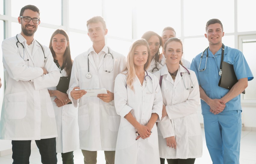 A group of eight medical professionals in white coats and scrubs stand together indoors, proudly smiling at the camera after excelling in their MCCQE1 exams, thanks to the comprehensive Ace QBank Update for MCCQE1.