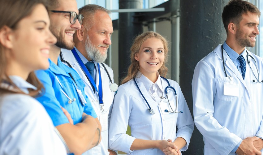 A group of five medical professionals in white coats and scrubs stand together in a well-lit room, smiling and looking ahead with confidence, perhaps after acing the MCCQE1.