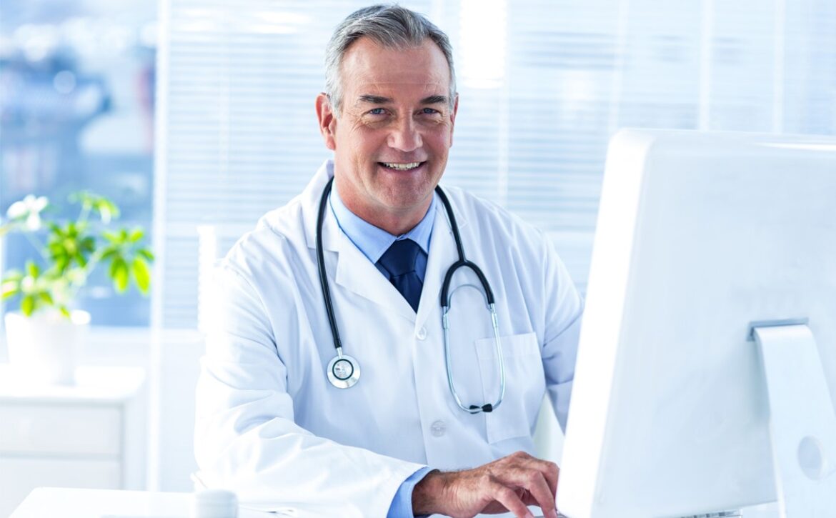 A doctor in a white coat with a stethoscope, seated at a desk, smiling at the camera in a well-lit office setting, confidently discusses strategies for MCCQE1 exam preparation and Ace QBank role.