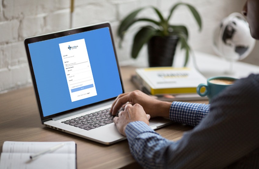 A person is using a laptop displaying a sign-in page for Ace QBank, perfect for MCCQE1 exam preparation. A notebook, pen, book, and cup are on the desk.