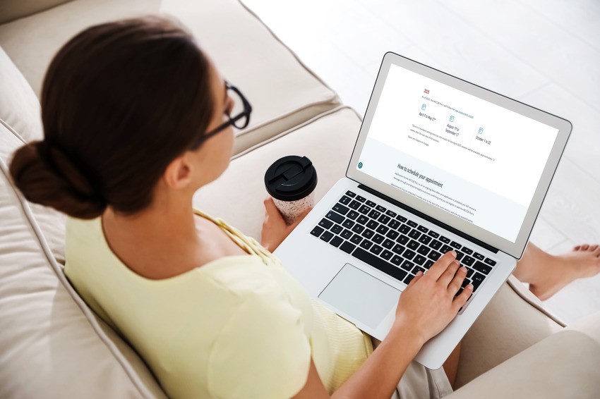 A person with a coffee cup is sitting on a couch using a laptop, exploring Ace QBank for MCCQE1 preparation while checking the upcoming MCCQE1 Exam Dates to register.