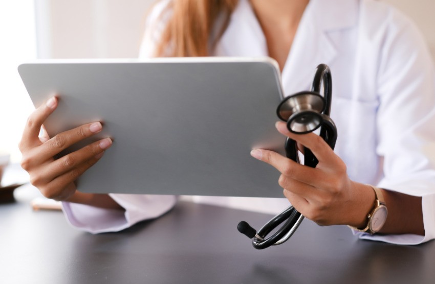 A person in a lab coat holds a tablet and a stethoscope, sitting at a desk, intently studying Ace QBank for MCCQE1 exam preparation.