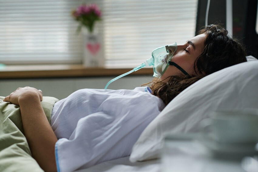 Young woman breathing with oxygen mask lying on bed during treatment in hospital-Ace QBank-Clinical edge