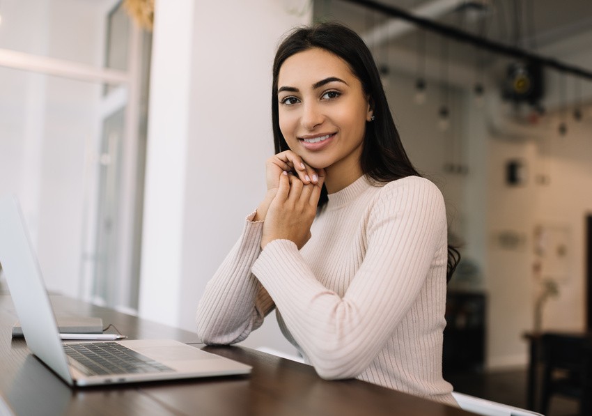 A person sits at a desk with a laptop, smiling confidently, as they explore Ace QBank's innovative AMC Exam Practice Strategies 2025 in a bustling office environment.